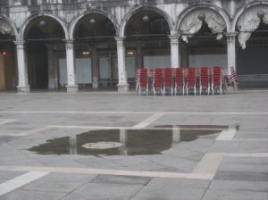 The tide doesn't come pouring over the battlements, but merely rises up through the storm drains.  This little pool will just keep expanding till it covers the Piazza.  After an hour or so, it will depart (tranquilly) by the same route.